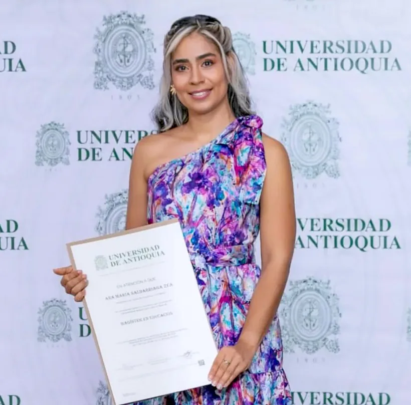 Ana María holding her Master's degree diploma at Universidad de Antioquia